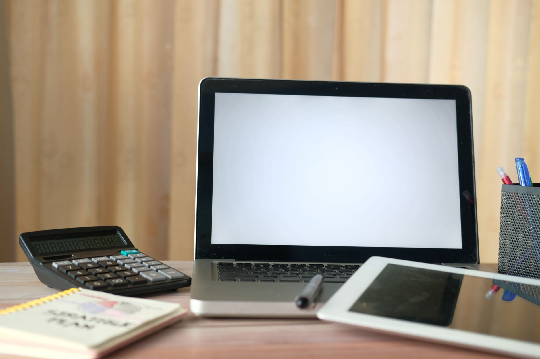 Laptop, Tablet, Taschenrechner und Notizbuch auf einem aufgeräumten Schreibtisch im Büro