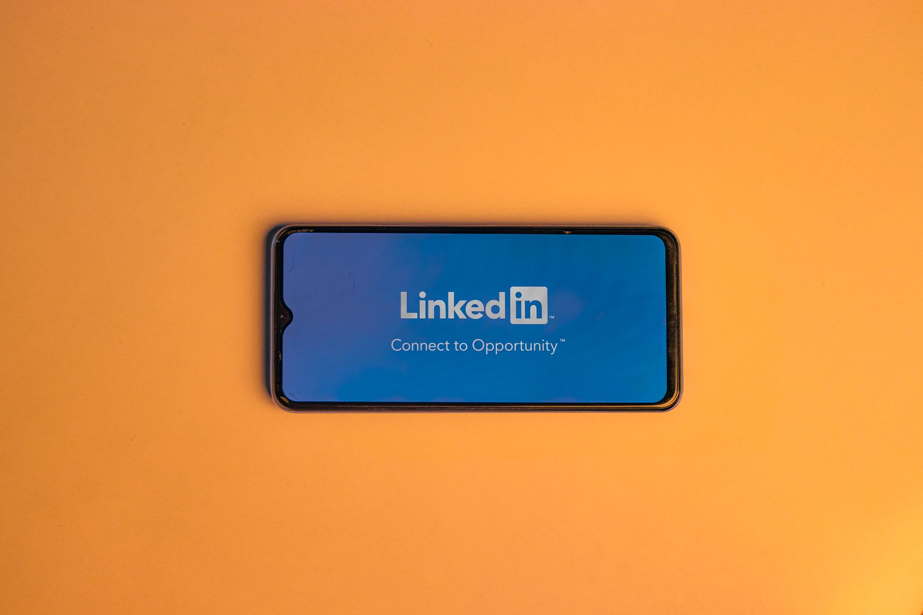 Smartphone mit geöffneter LinkedIn-App liegt auf orangefarbenem Hintergrund