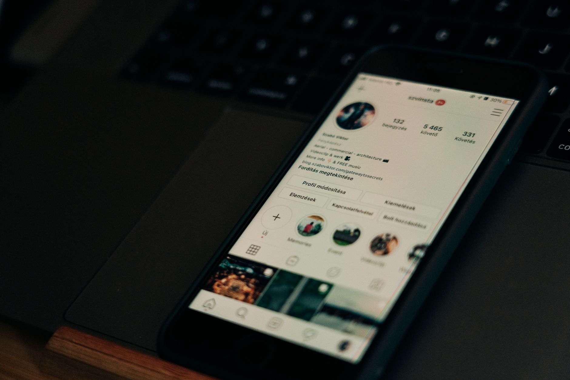 Smartphone mit Instagram-Profilansicht liegt auf einem Laptop im abgedunkelten Büro